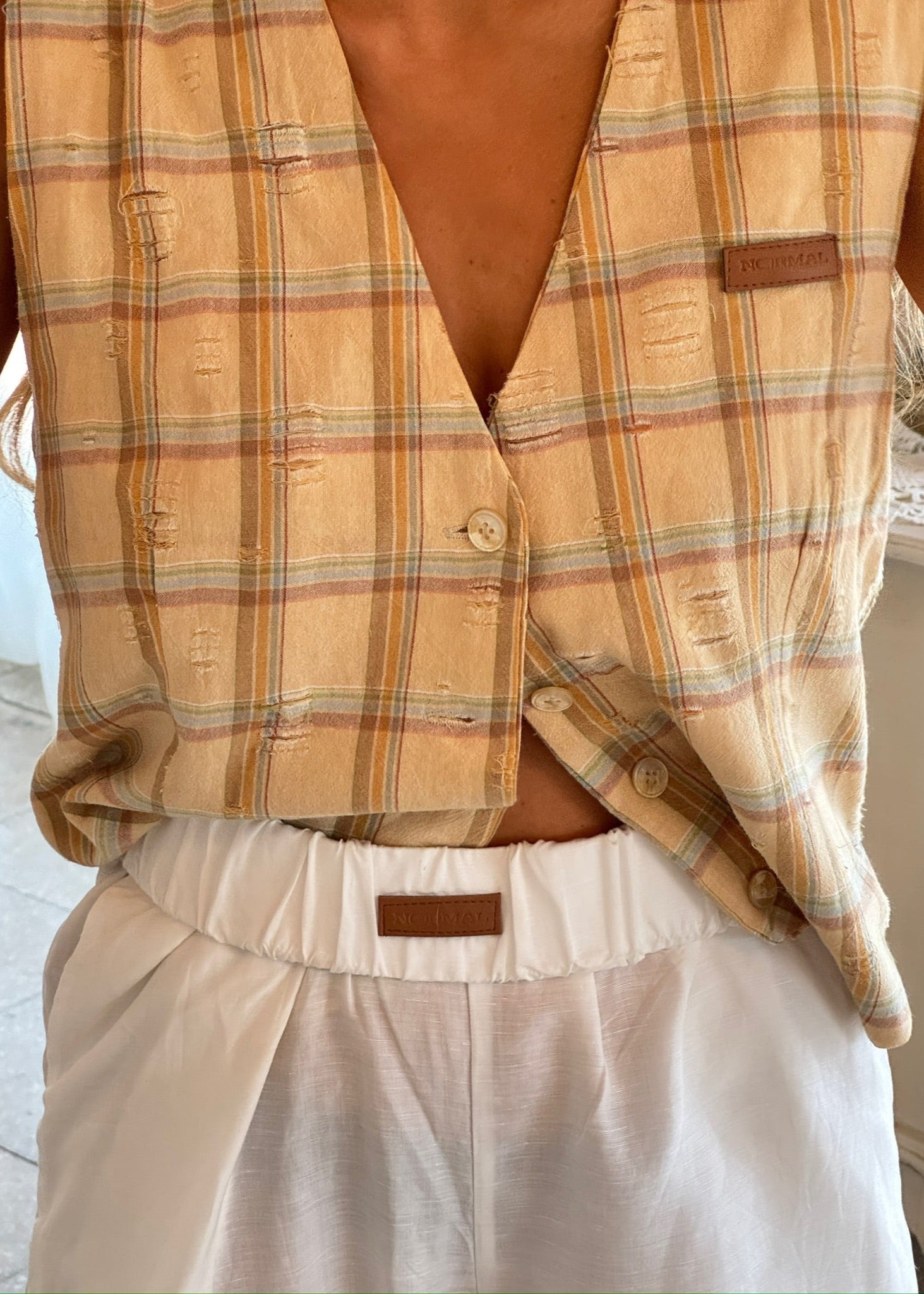Person wearing a plaid vest over a white shirt with a visible brand logo.