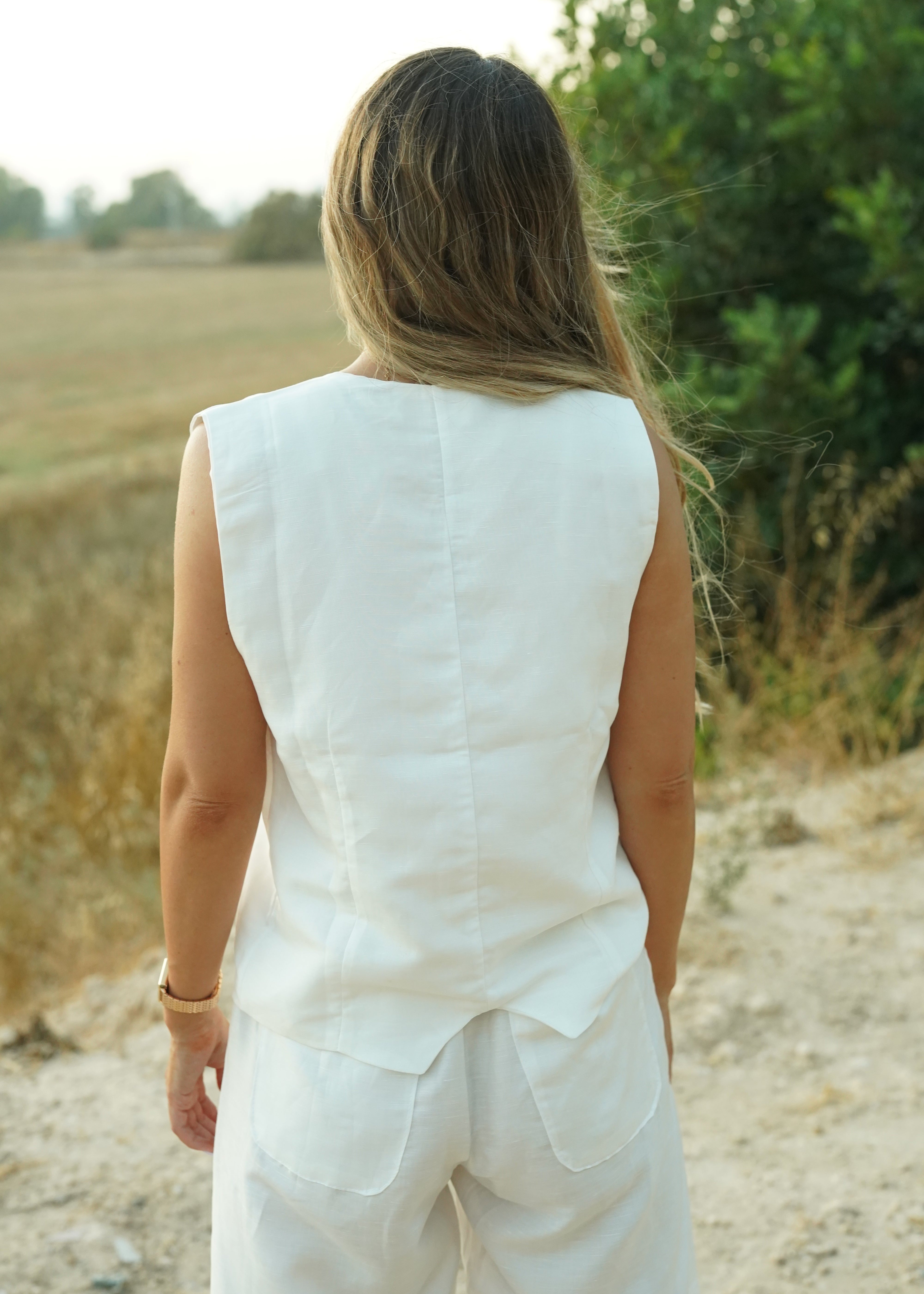 Woman in a white dress standing outdoors with greenery in the background