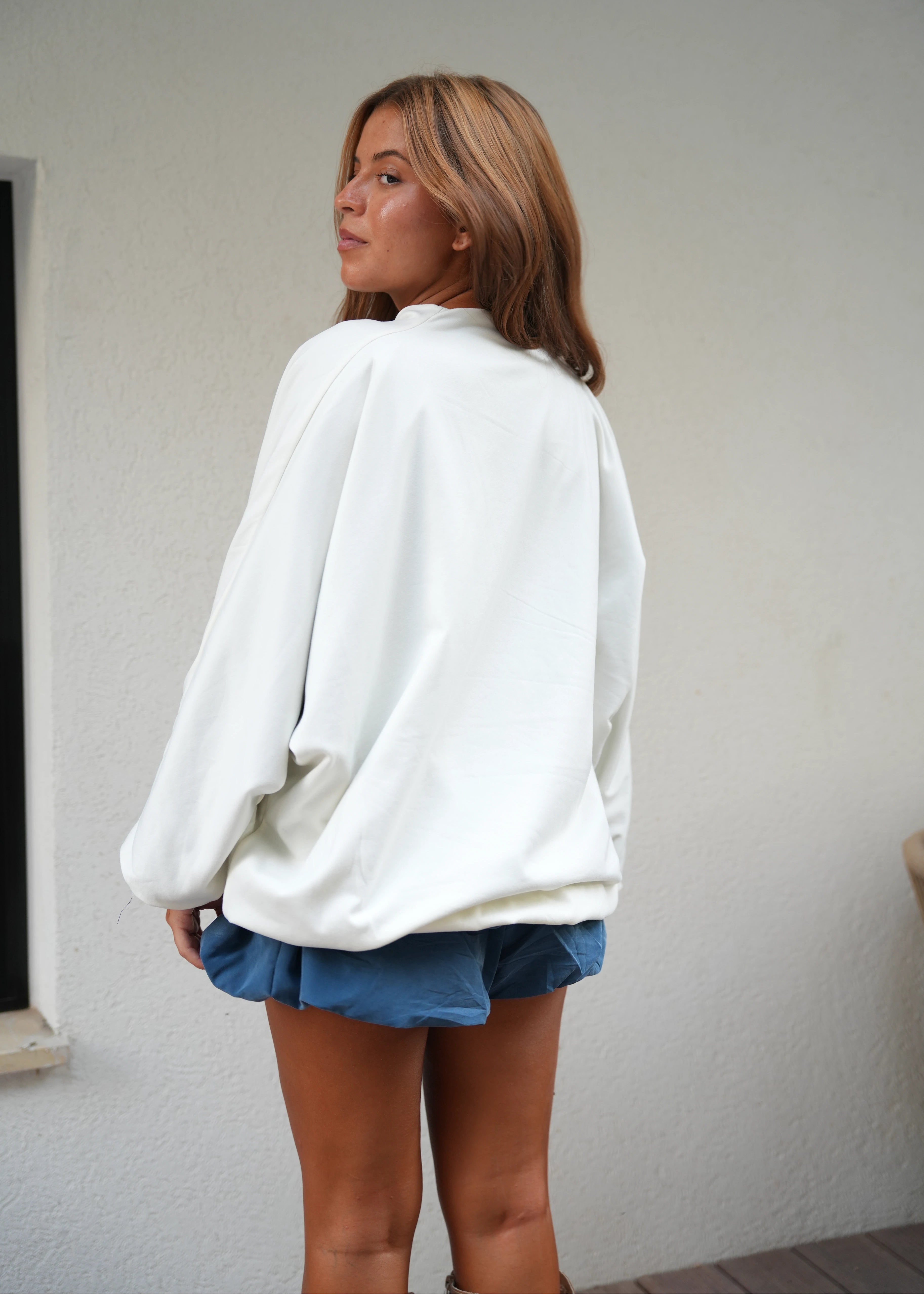 Person wearing a white sweater and blue shorts on a plain background
