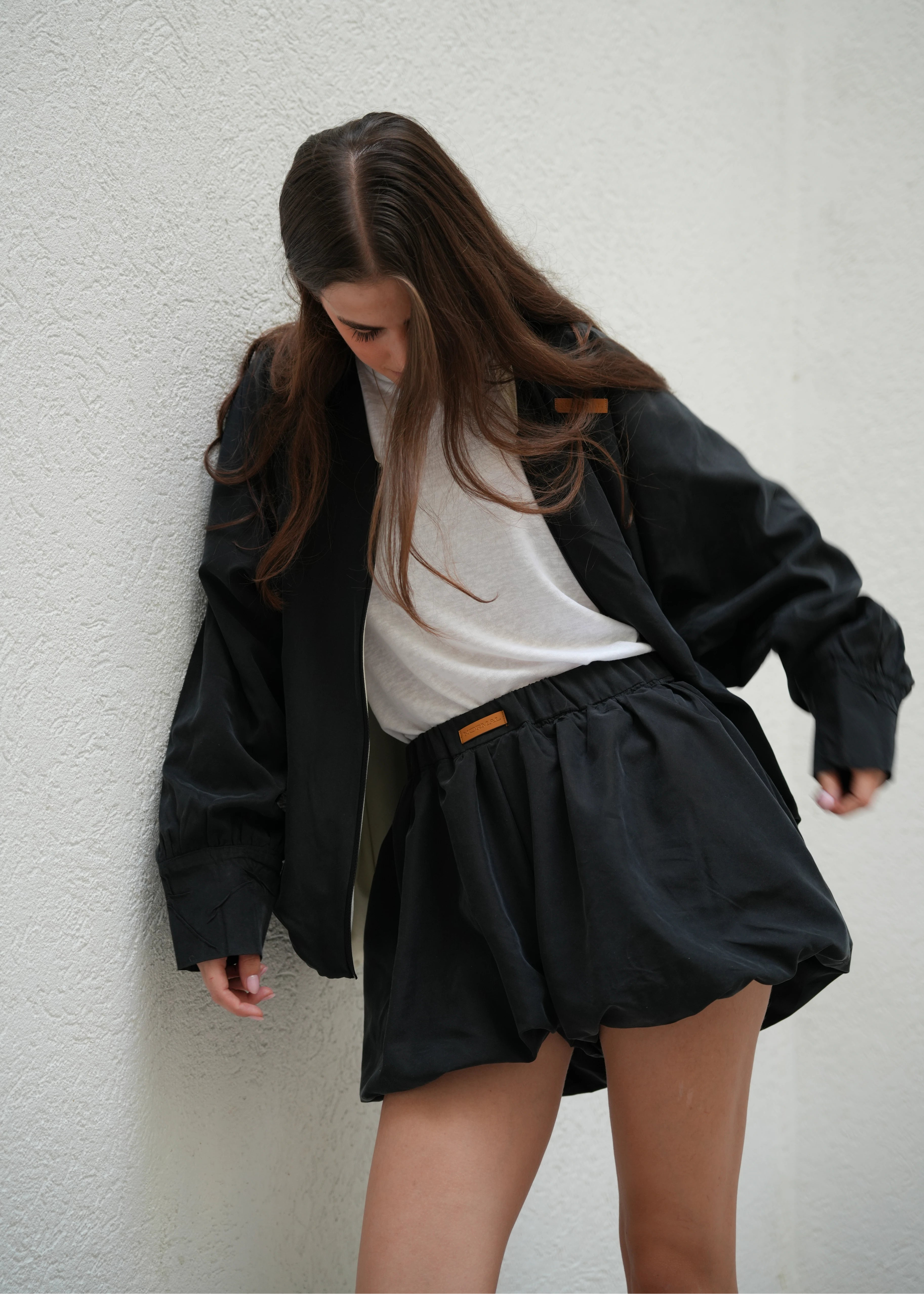 Person wearing a black outfit with a white shirt underneath on a plain background