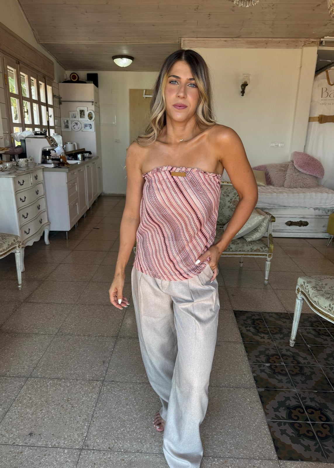 Woman standing in a kitchen wearing a strapless pink top and light-colored pants.