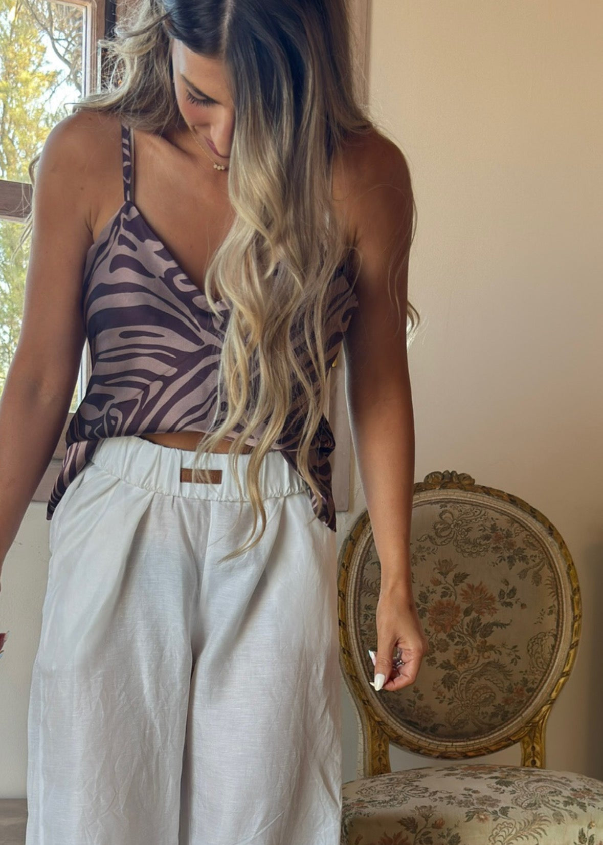 Woman wearing a zebra print top and light-colored pants in a room with a decorative chair.