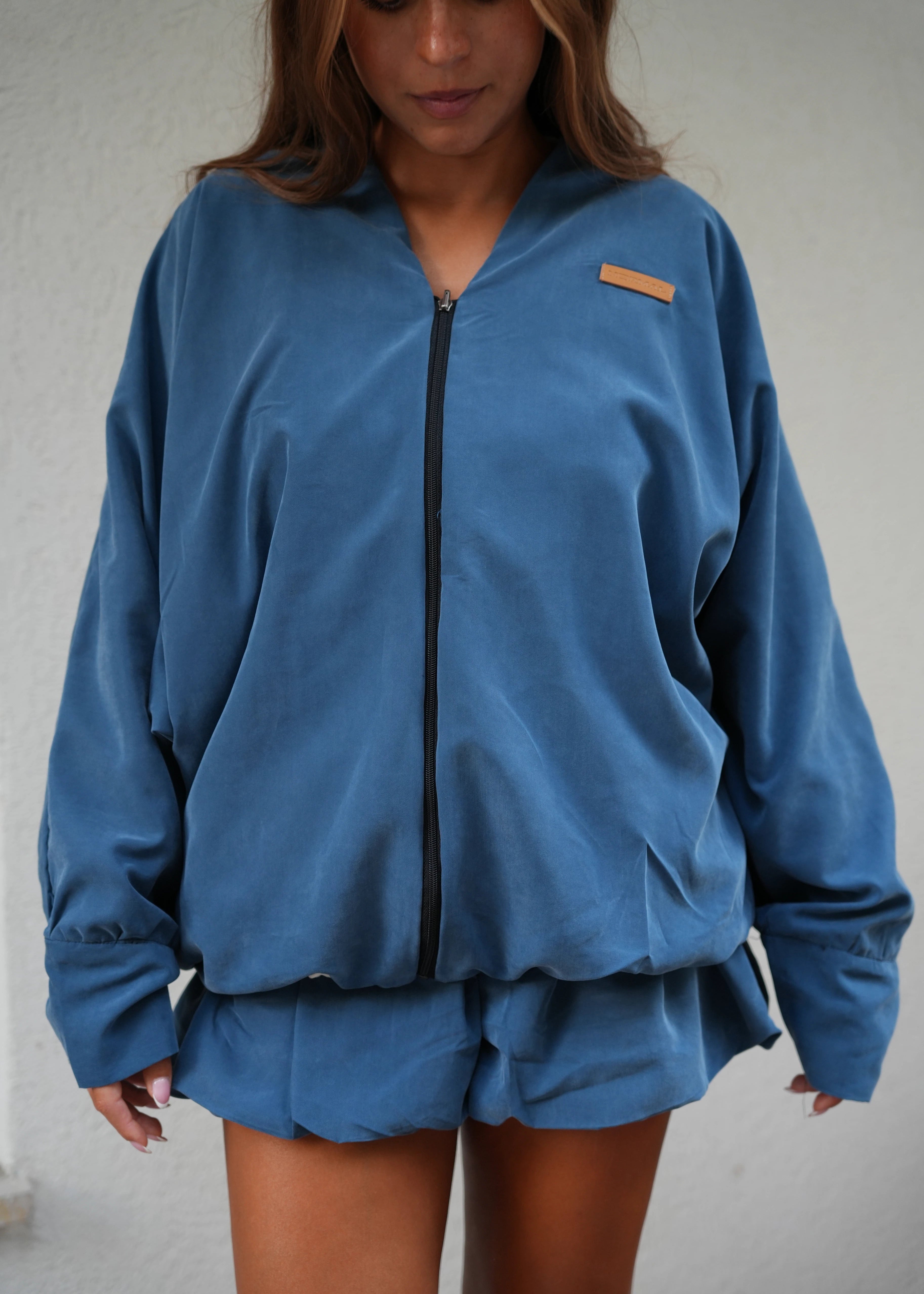 Person wearing a blue jacket with a brand logo on a plain background